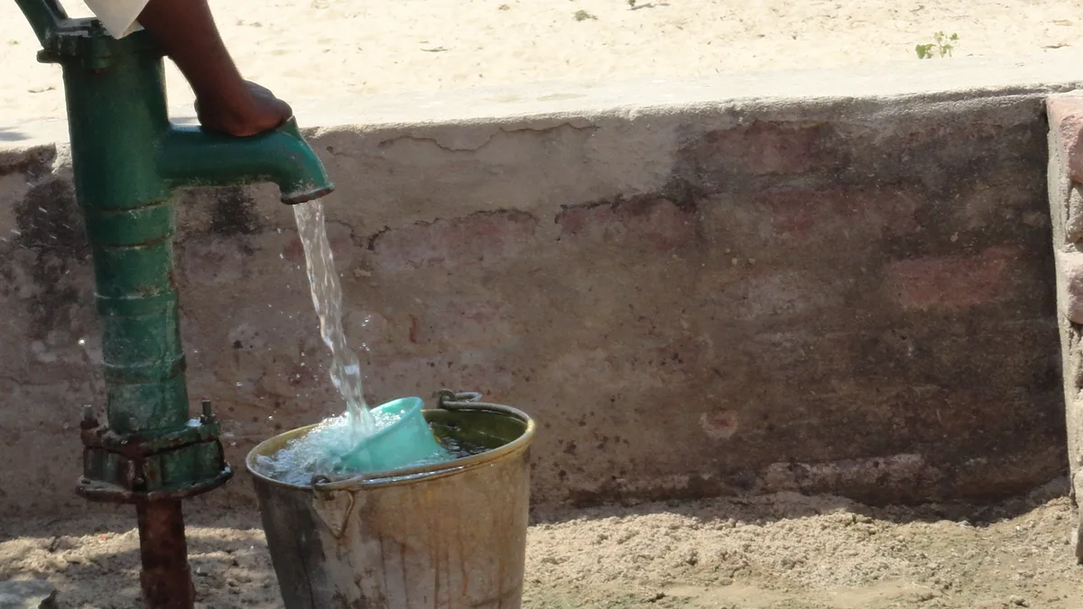 Water pouring from a green hand pump into a metal bucket