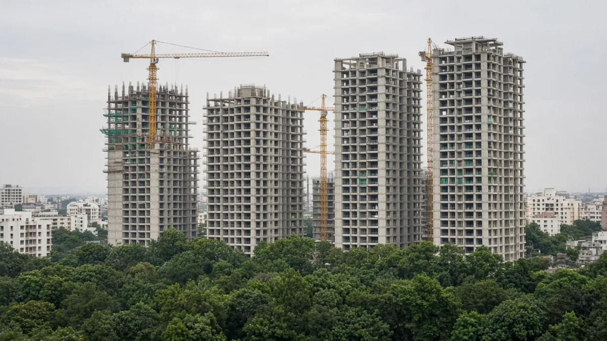 Apartment towers under construction with cranes above treetops