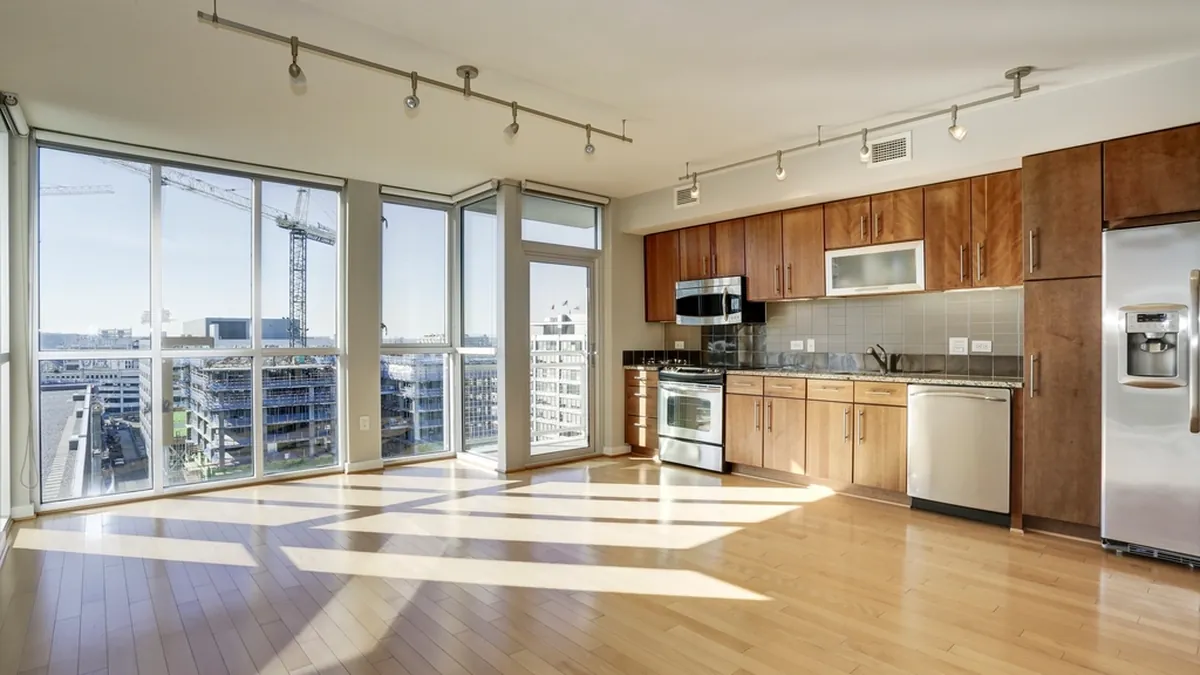 An empty apartment with wooden flooring, an open kitchen and tall windows